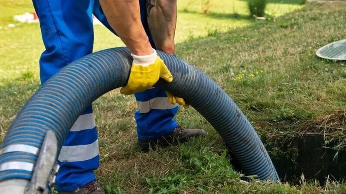 Operador com mangueira de sucção em serviço de limpeza de fossa séptica em área gramada